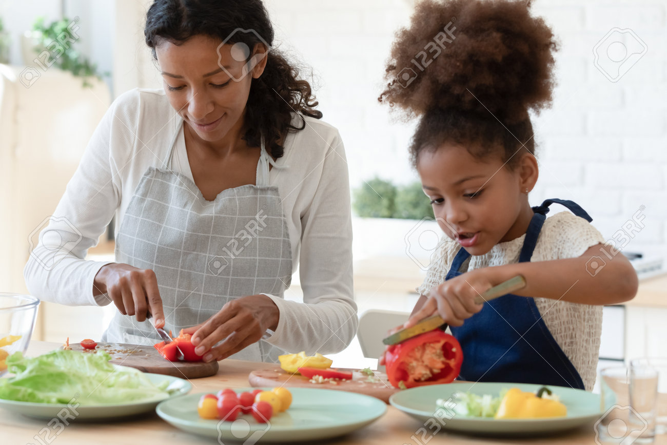 Happy mommy and cute daughter girl in aprons cooking together in kitchen. Mom and kid slicing fresh vegetables for salad, preparing healthy organic meal and talking. Family eating at home concept - 168073906 Happy mommy and cute daughter girl in aprons cooking together in kitchen. Mom and kid slicing fresh vegetables for salad, preparing healthy organic meal and talking. Family eating at home concept - 168073906
