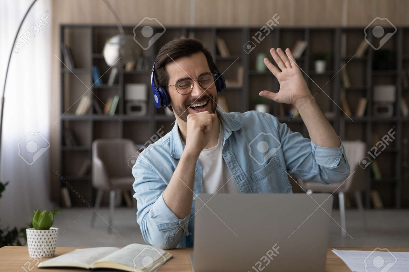 Funny Motivation. Carefree Young Guy Employee Wear Headset Relax From  Computer Work Sing Song To Imaginary Microphone In Hand Relieve Stress.  Happy Millennial Man Melomane Listen To Music Online On Pc Stock, image size:1300x867