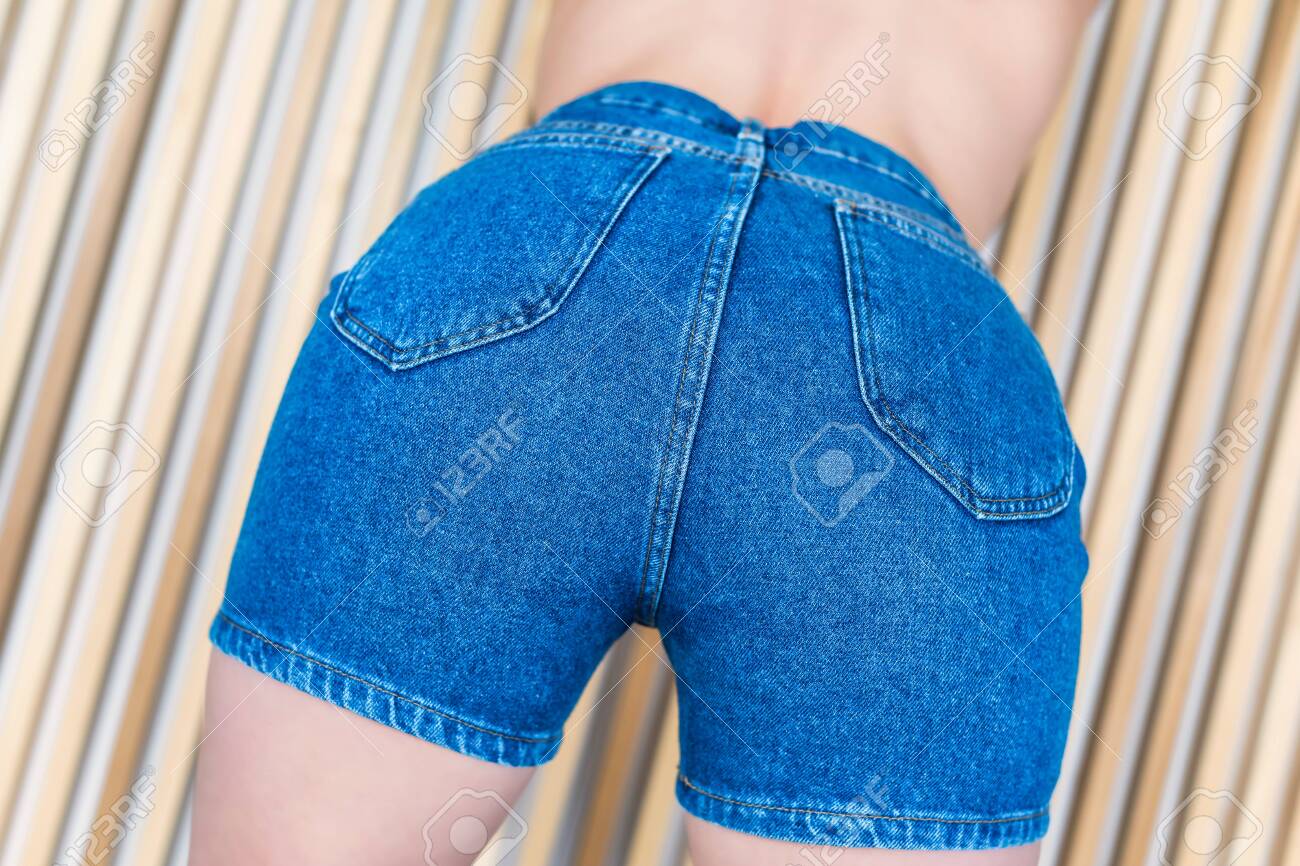 Bottom view on women's in denim shorts on the background of wooden beams - 124871661 Bottom view on women's in denim shorts on the background of wooden beams - 124871661