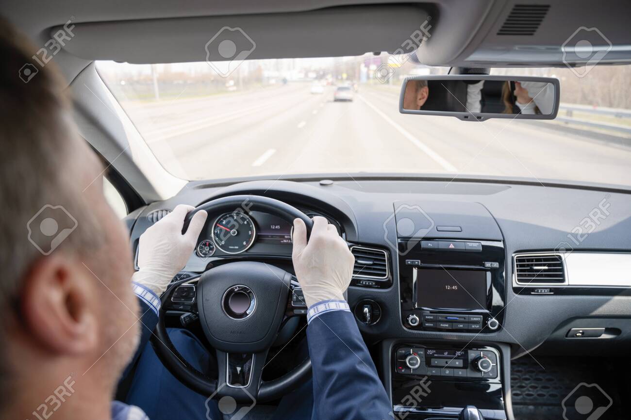 Middle age businessman in a blue suit and rubber gloves for protect himself from bacteria and virus driving a car. Coronavirus. Pandemic. - 145053017 Middle age businessman in a blue suit and rubber gloves for protect himself from bacteria and virus driving a car. Coronavirus. Pandemic. - 145053017