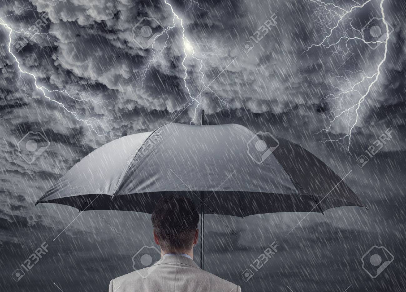 Businessman with black business umbrella protecting himself from the storm concept for insurance, financial protection from recession or economic depression - 54428257 Businessman with black business umbrella protecting himself from the storm concept for insurance, financial protection from recession or economic depression - 54428257