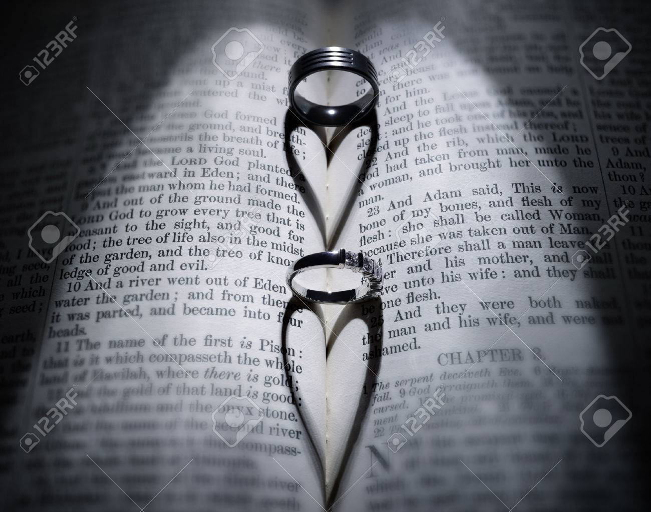 wedding rings casting heart shaped shadow over bible stock photo