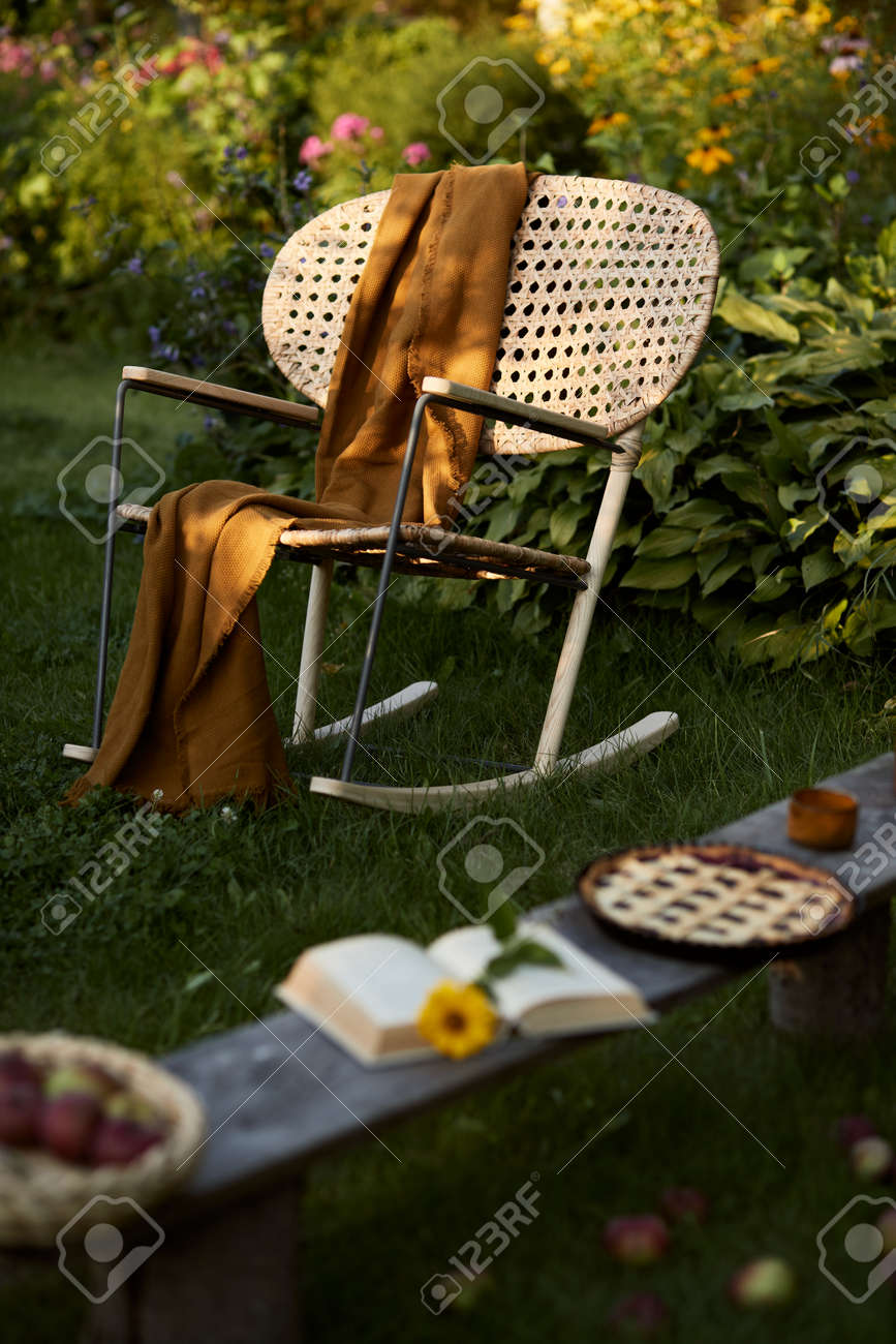 Stylish composition of countryside garden with design rattan armchair, wooden bench, plaid, food, drinks and elegant accessories. A lot of colorful flowers. Summer mood. - 168356136 Stylish composition of countryside garden with design rattan armchair, wooden bench, plaid, food, drinks and elegant accessories. A lot of colorful flowers. Summer mood. - 168356136