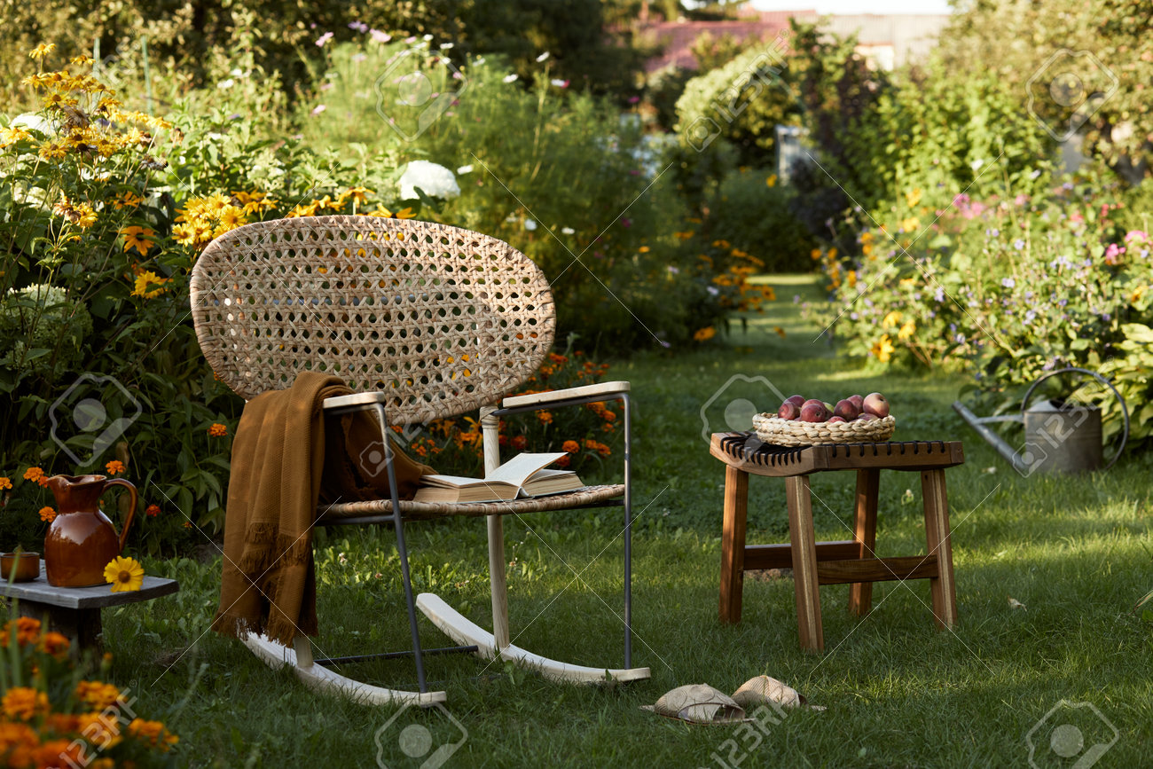 Stylish composition of countryside garden with design rattan armchair, wooden bench, plaid, food, drinks and elegant accessories. A lot of colorful flowers. Summer mood. - 168356329 Stylish composition of countryside garden with design rattan armchair, wooden bench, plaid, food, drinks and elegant accessories. A lot of colorful flowers. Summer mood. - 168356329