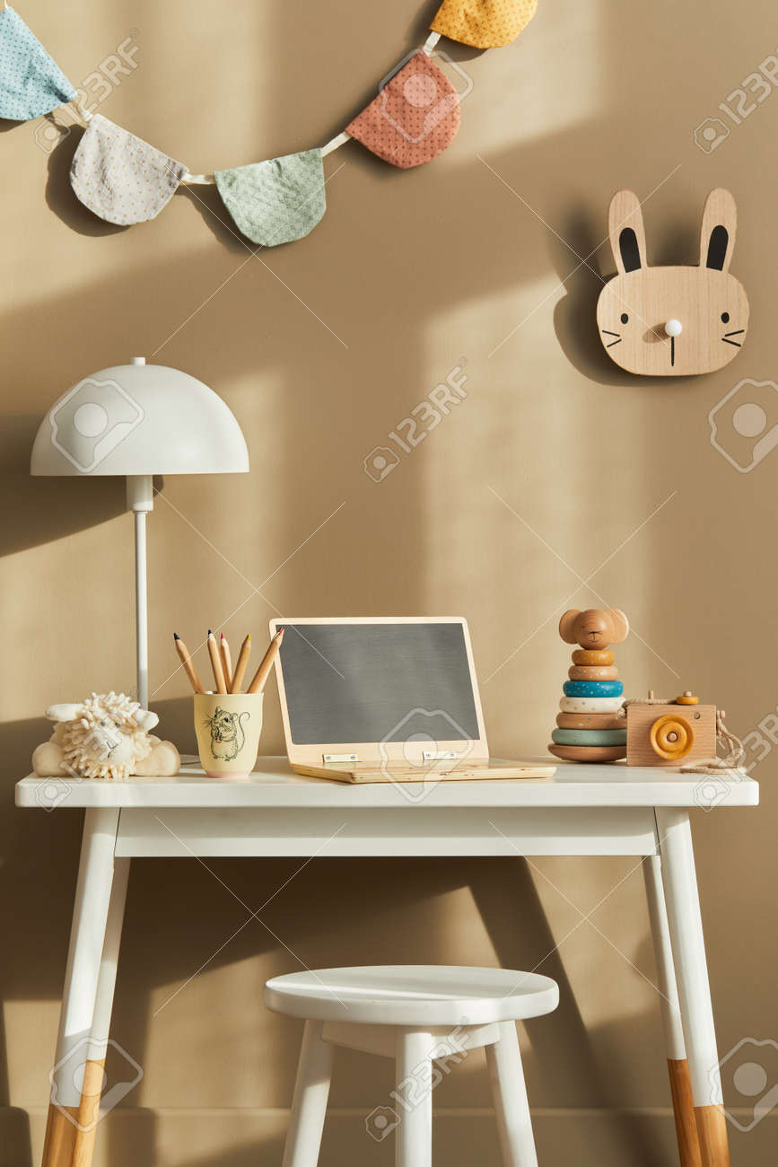 Interior design of stylish kid room space with white desk, wooden laptop, toys, child accessories, lamp, cozy decoration and hanging cotton flags on the beige wall. Template. - 168356383 Interior design of stylish kid room space with white desk, wooden laptop, toys, child accessories, lamp, cozy decoration and hanging cotton flags on the beige wall. Template. - 168356383