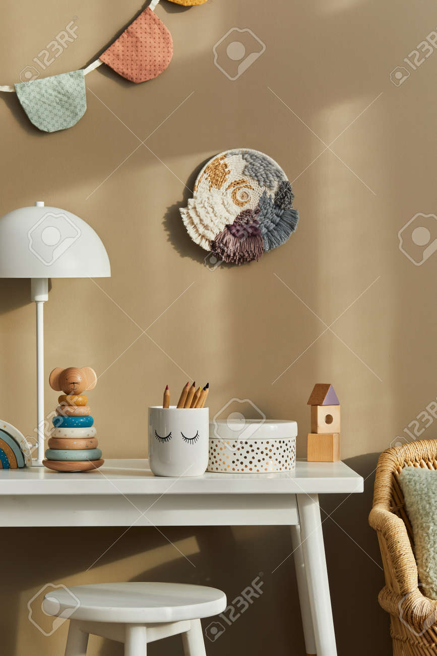 Interior design of stylish kid room space with white desk, wooden toys, child accessories, white lamp, cozy decoration and hanging cotton flags on the beige wall. Template. - 168356726 Interior design of stylish kid room space with white desk, wooden toys, child accessories, white lamp, cozy decoration and hanging cotton flags on the beige wall. Template. - 168356726
