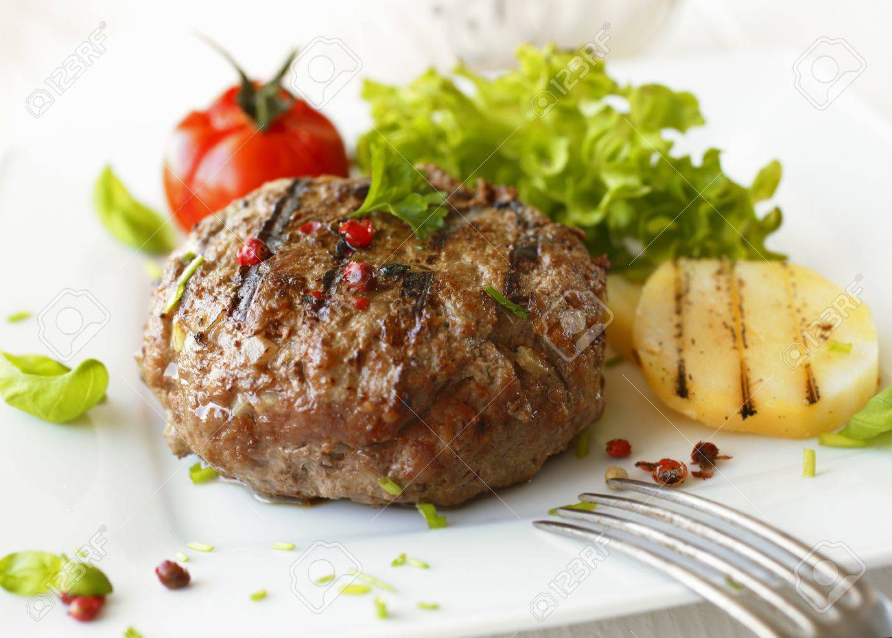 Delicious grilled beef meatball served on a white plate with tomato and lettuce with a fork in the foreground - 18995415 Delicious grilled beef meatball served on a white plate with tomato and lettuce with a fork in the foreground - 18995415
