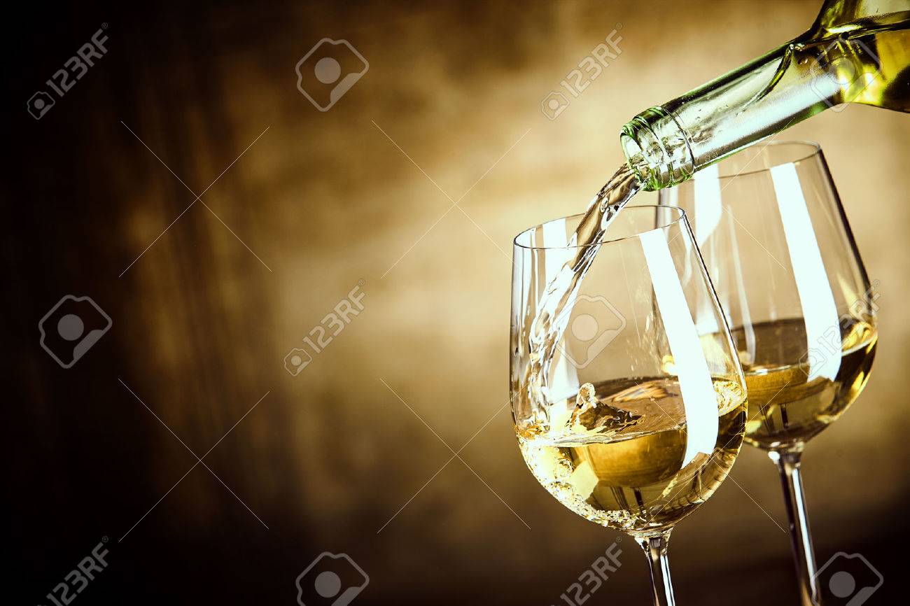 Pouring two glasses of white wine from a bottle in a close up view of the wineglasses over an abstract brown blue background with copy space - 57259324 Pouring two glasses of white wine from a bottle in a close up view of the wineglasses over an abstract brown blue background with copy space - 57259324