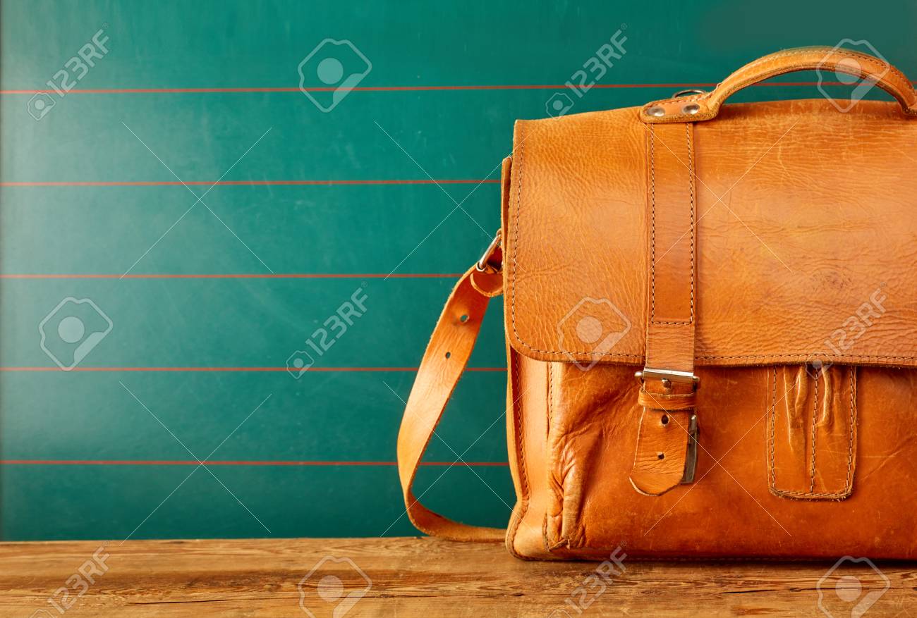 Closed leather backpack case with copy space over green wall and old wooden table - 105071939 Closed leather backpack case with copy space over green wall and old wooden table - 105071939
