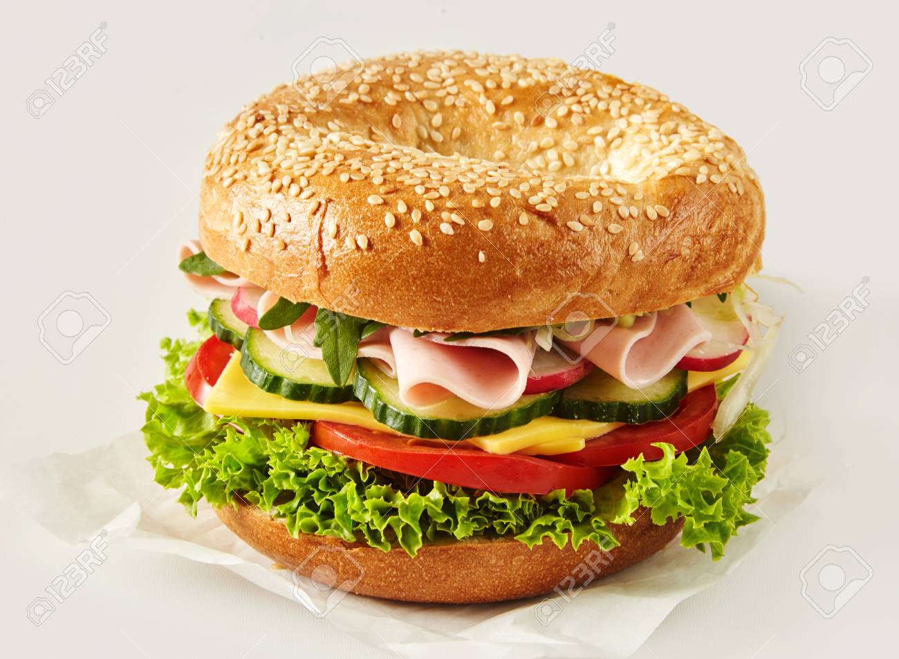 Crusty sesame bun or bagel with ham, cheese and salad filling on paper over white for advertising or a menu - 106485564 Crusty sesame bun or bagel with ham, cheese and salad filling on paper over white for advertising or a menu - 106485564