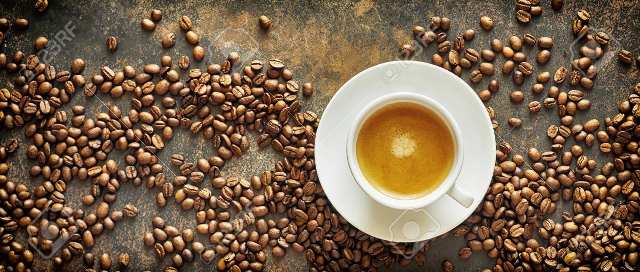 Panorama banner with roasted coffee beans and a generic white cup and saucer of milky latte coffee on a textured slate background viewed from above - 110778282 Panorama banner with roasted coffee beans and a generic white cup and saucer of milky latte coffee on a textured slate background viewed from above - 110778282