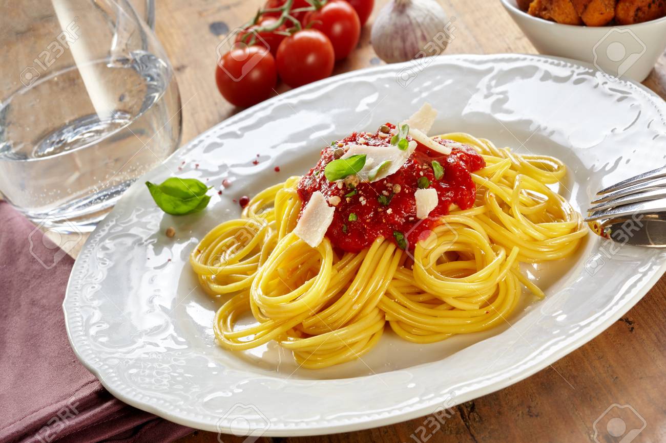 Plate of spaghetti Bolognaise or Bolognese with a tomato and herb topping sprinkled wth parmesan cheese in a tilted view on a wooden table - 115257795 Plate of spaghetti Bolognaise or Bolognese with a tomato and herb topping sprinkled wth parmesan cheese in a tilted view on a wooden table - 115257795