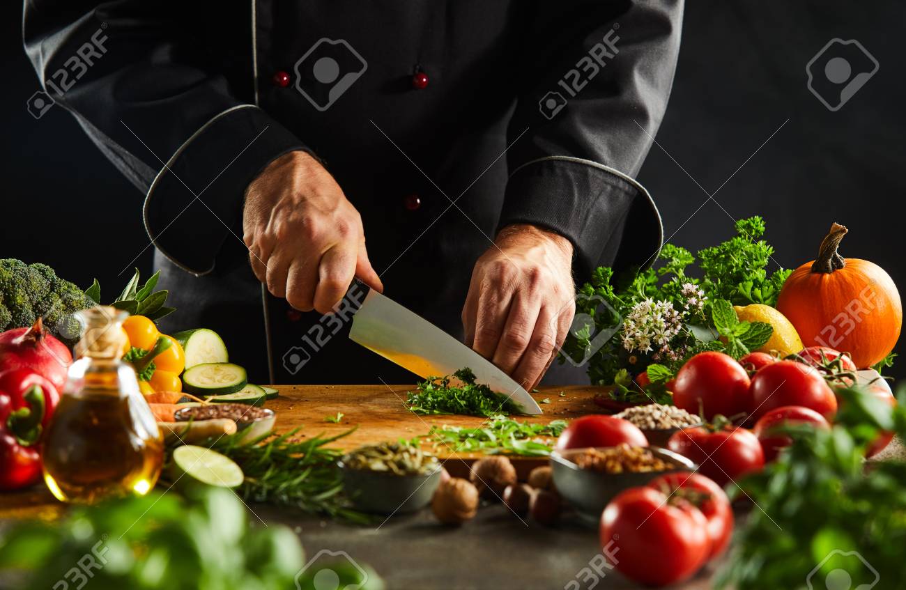 Chef dicing fresh herbs on a wooden chopping board with a kitchen knife while preparing salad in a close up on the hands - 115257958 Chef dicing fresh herbs on a wooden chopping board with a kitchen knife while preparing salad in a close up on the hands - 115257958