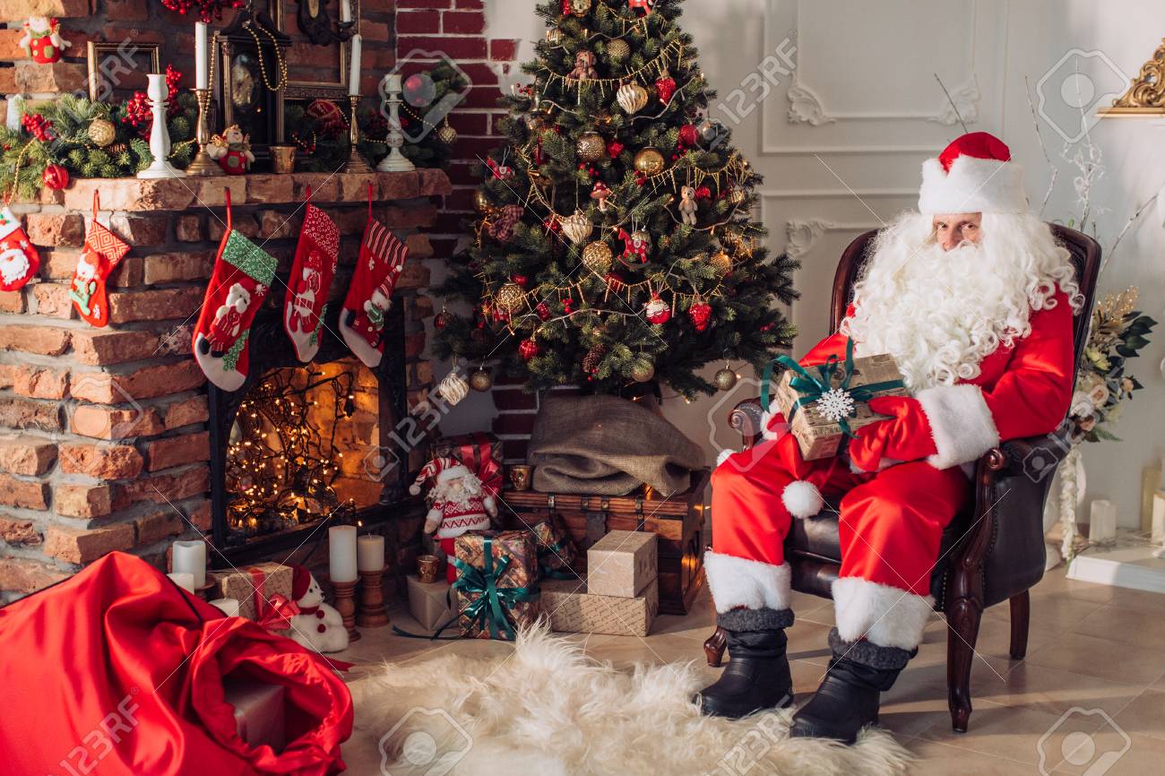 クリスマスツリーと暖炉の近くの彼の部屋に座っているサンタクロースの肖像画 の写真素材 画像素材 Image
