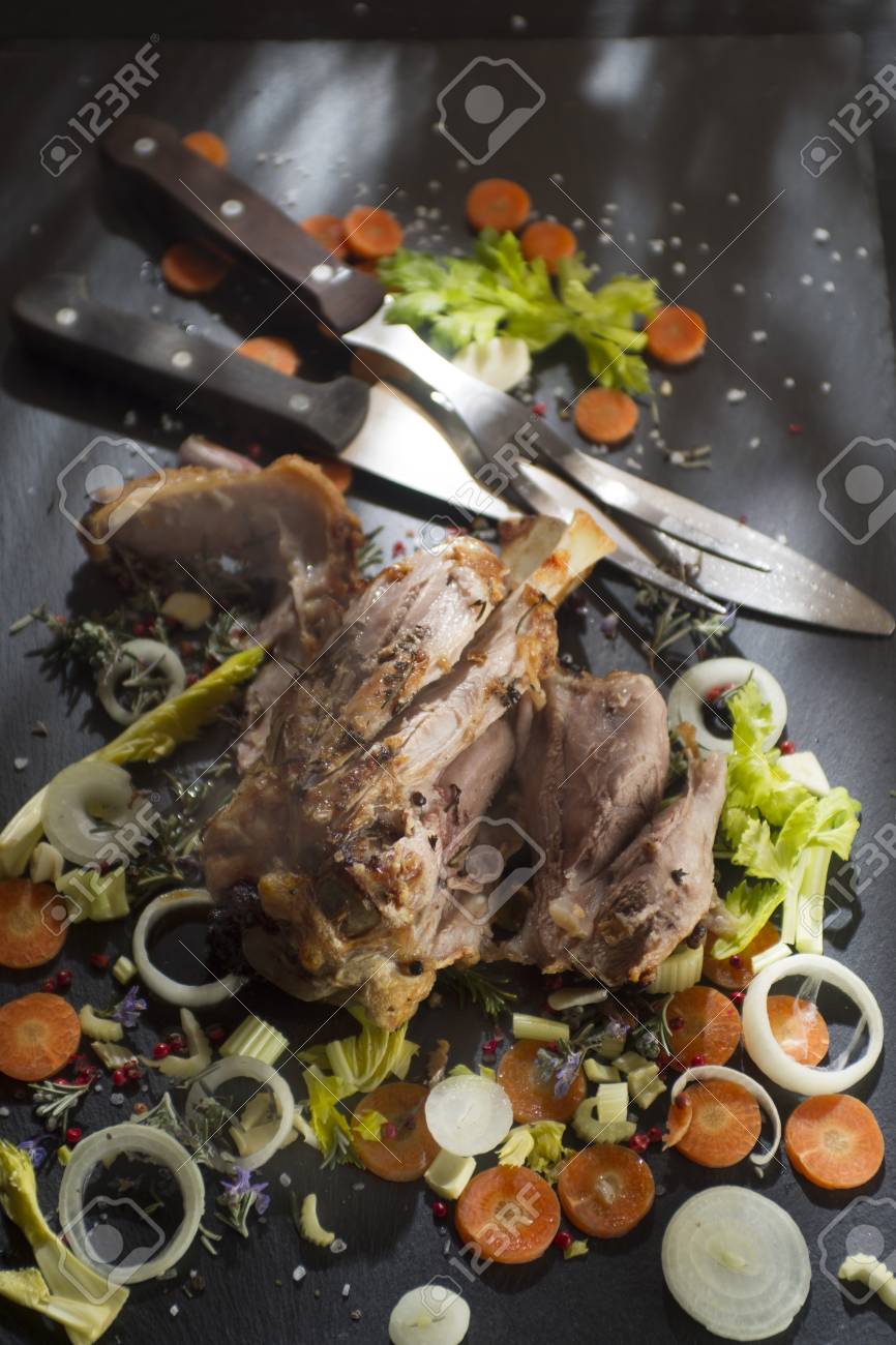 presentation of a cooked pork shank with vegetables on stone stock slate presentation