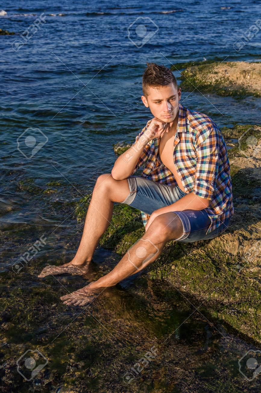 海の水の近くの岩の上に座って魅力的な若者のファッションのセクシーな男 の写真素材 画像素材 Image