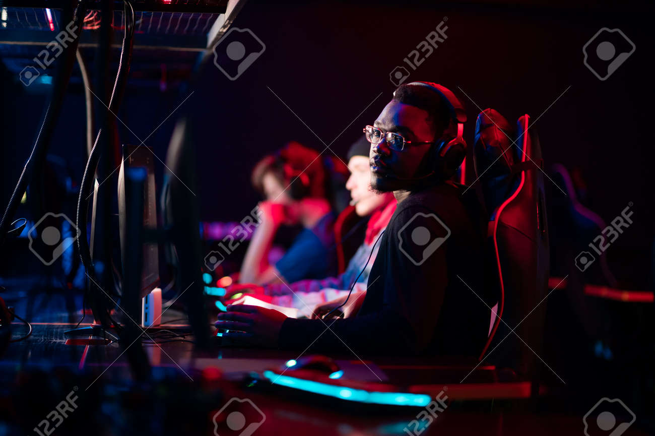 A member of the esports team at a bootcamp training session. Portrait of a black guy with glasses at a gaming computer with a glowing keyboard. - 170401109 A member of the esports team at a bootcamp training session. Portrait of a black guy with glasses at a gaming computer with a glowing keyboard. - 170401109