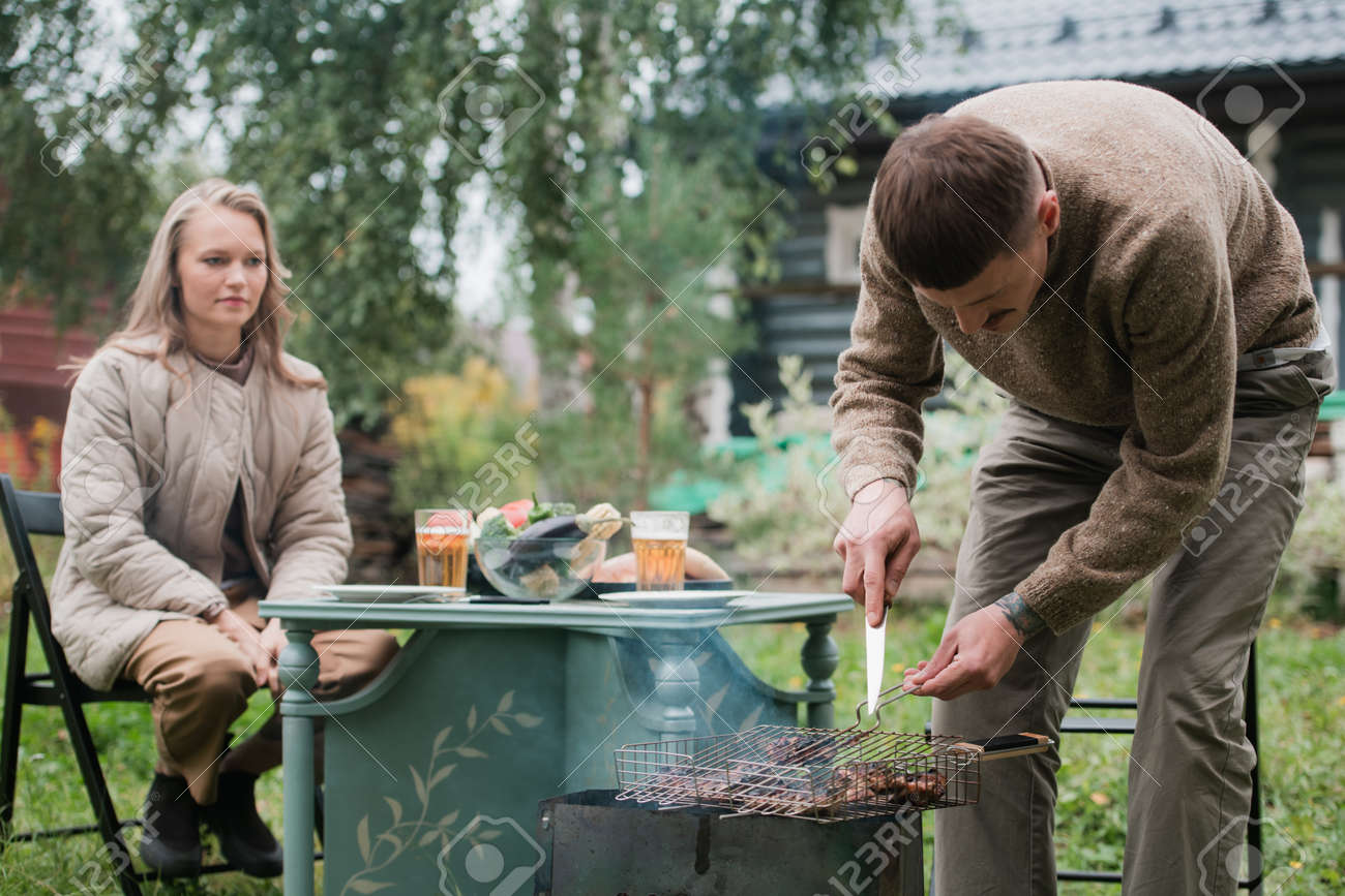 A young eastern european man prepares a barbecue, roasts fragrant meat on the grill. Concept of a romantic picnic for a young couple. - 170401053 A young eastern european man prepares a barbecue, roasts fragrant meat on the grill. Concept of a romantic picnic for a young couple. - 170401053