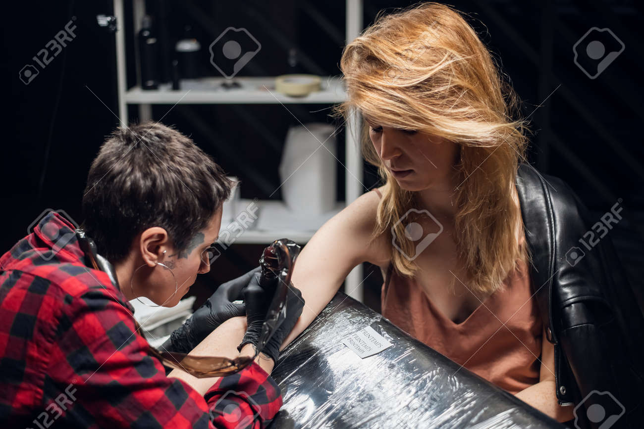 A young red-haired girl came to the tattoo artist in the salon to make the first tattoo in her life on her face. The master is a girl with tattoos on her face and body. - 170401060 A young red-haired girl came to the tattoo artist in the salon to make the first tattoo in her life on her face. The master is a girl with tattoos on her face and body. - 170401060