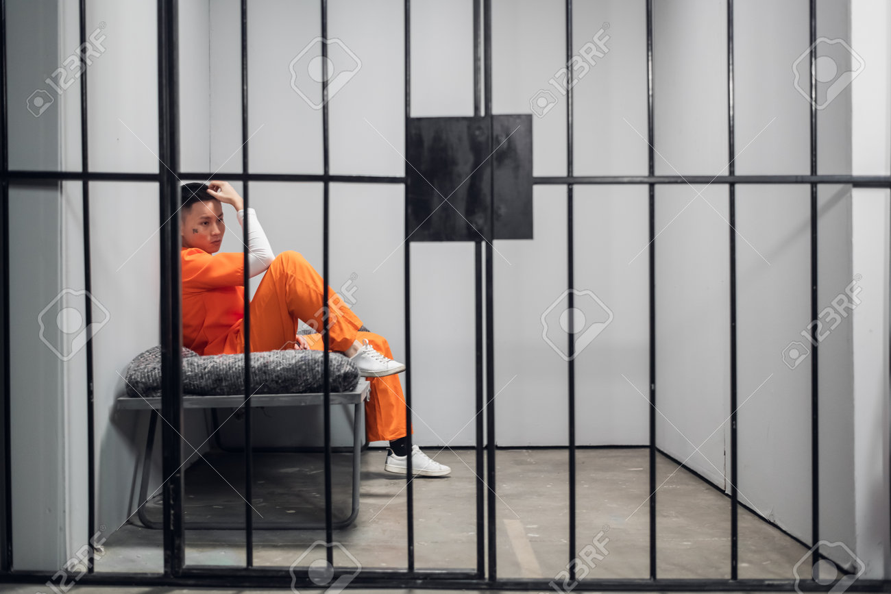Asian criminal with tattoos on his face in a cell repents of the crime. Depression of a prisoner in prison. - 170401003 Asian criminal with tattoos on his face in a cell repents of the crime. Depression of a prisoner in prison. - 170401003