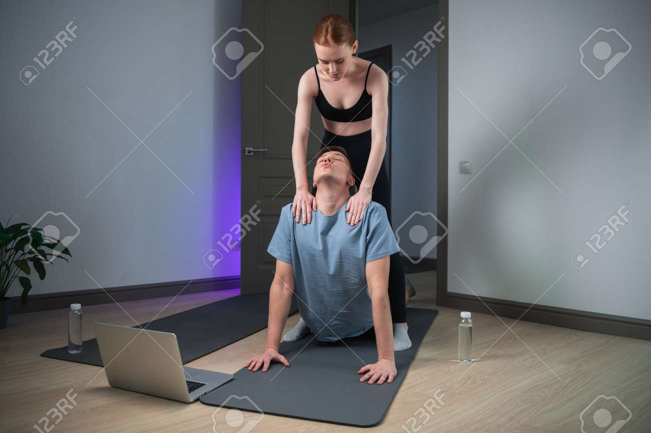 The upward-facing dog asana the most popular asana in yoga, an experienced trainer helps a woman to do it to a man at home - 170401013 The upward-facing dog asana the most popular asana in yoga, an experienced trainer helps a woman to do it to a man at home - 170401013