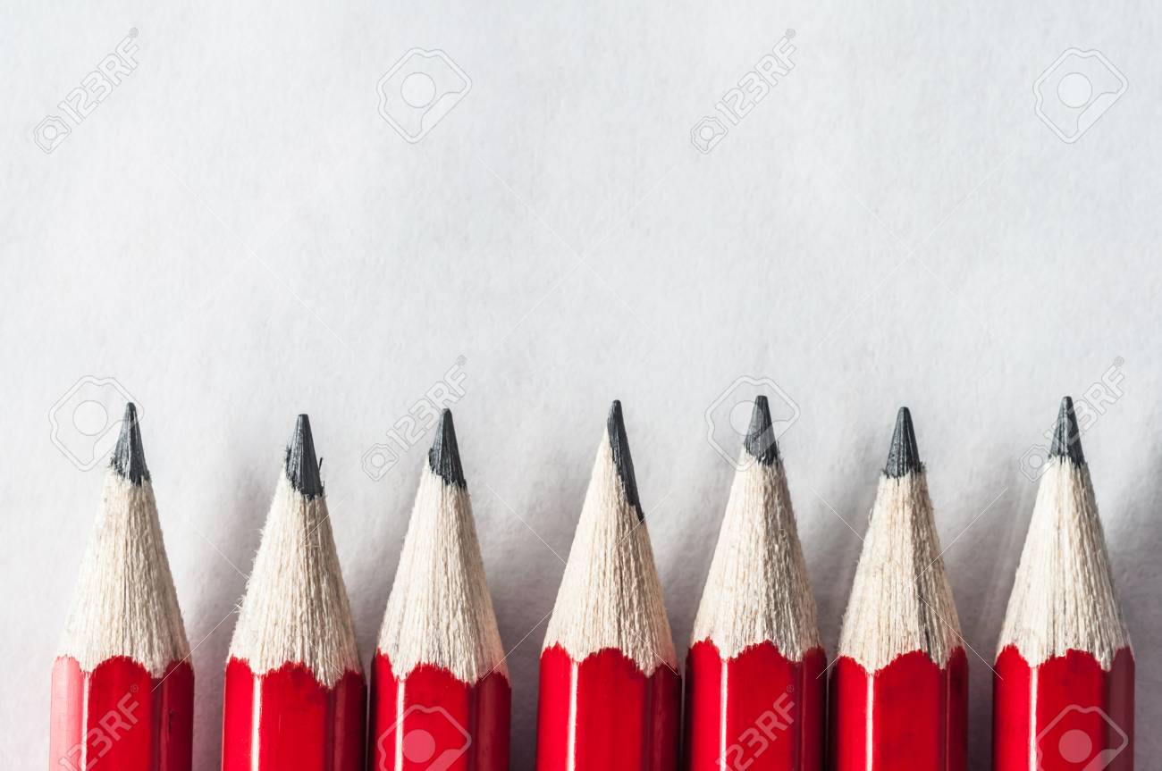 a row of roughly sharpened grubby red pencils on textured art