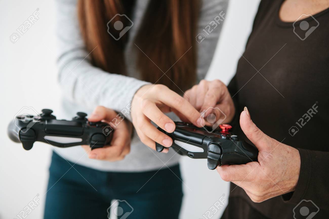 若い女の子は ビデオゲームのためにジョイスティックを使用する方法を高齢の女性に説明します 共同気晴らし 現代の技術と人々 孫娘と祖母のコミュニケーション の写真素材 画像素材 Image