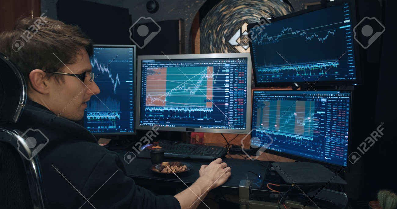 男性トレーダー、証券取引所のフリーランサーはオプションを取引し、ナッツを食べます。画面上の相場の成長と下降のチャート。株式、先物、債券を取引するための証券取引所でのゲームの概念の写真素材・画像素材  Image 183024490