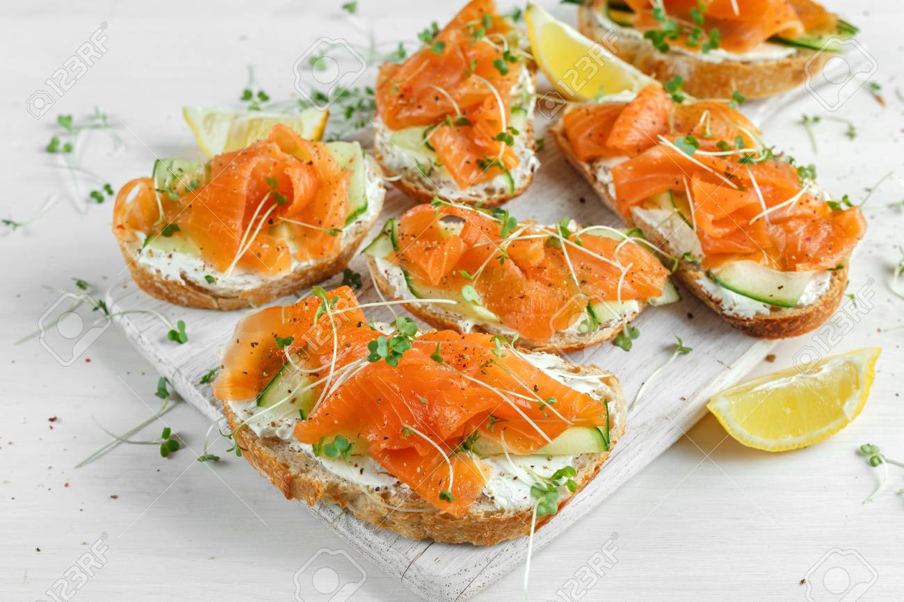 Smoked salmon bruschettas with soft cheese and cucumber shavings on white board. - 77624351 Smoked salmon bruschettas with soft cheese and cucumber shavings on white board. - 77624351