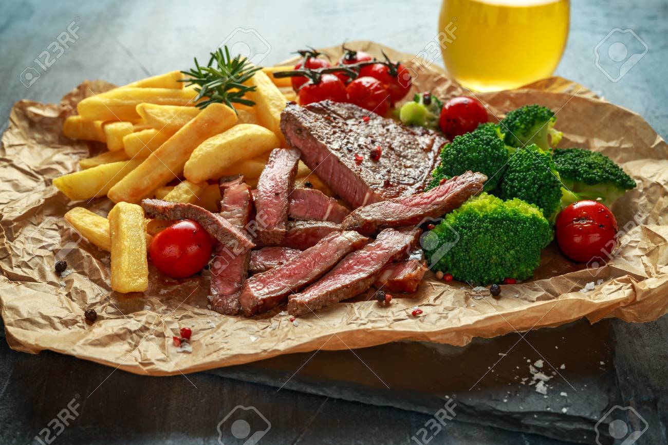 Grilled sirloin steak with potato fries, broccoli, beer and cherry tomatoes on crumpled paper - 108608821 Grilled sirloin steak with potato fries, broccoli, beer and cherry tomatoes on crumpled paper - 108608821