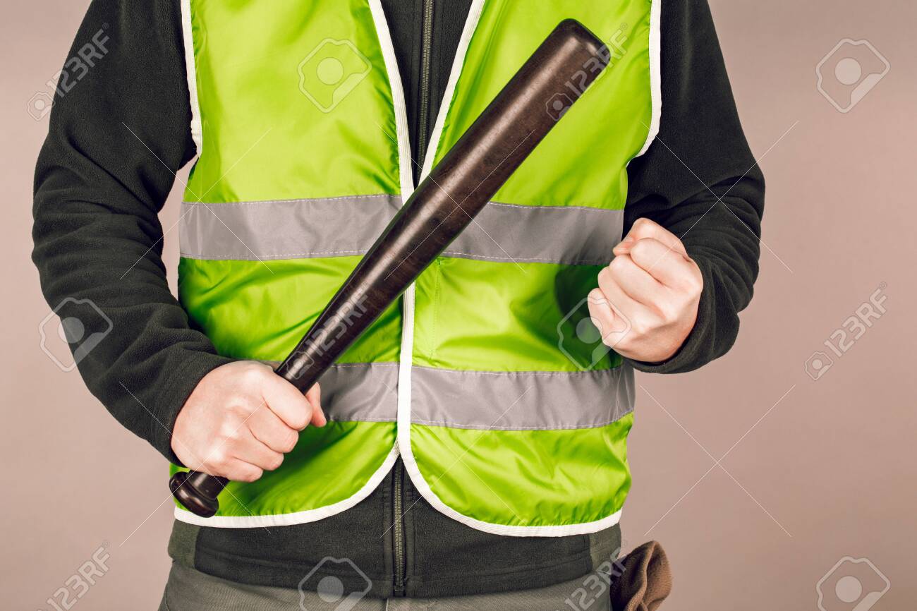 man in a yellow vest, a Builder or a protester with a baseball bat in his hands on a gray background. - 126139635 man in a yellow vest, a Builder or a protester with a baseball bat in his hands on a gray background. - 126139635