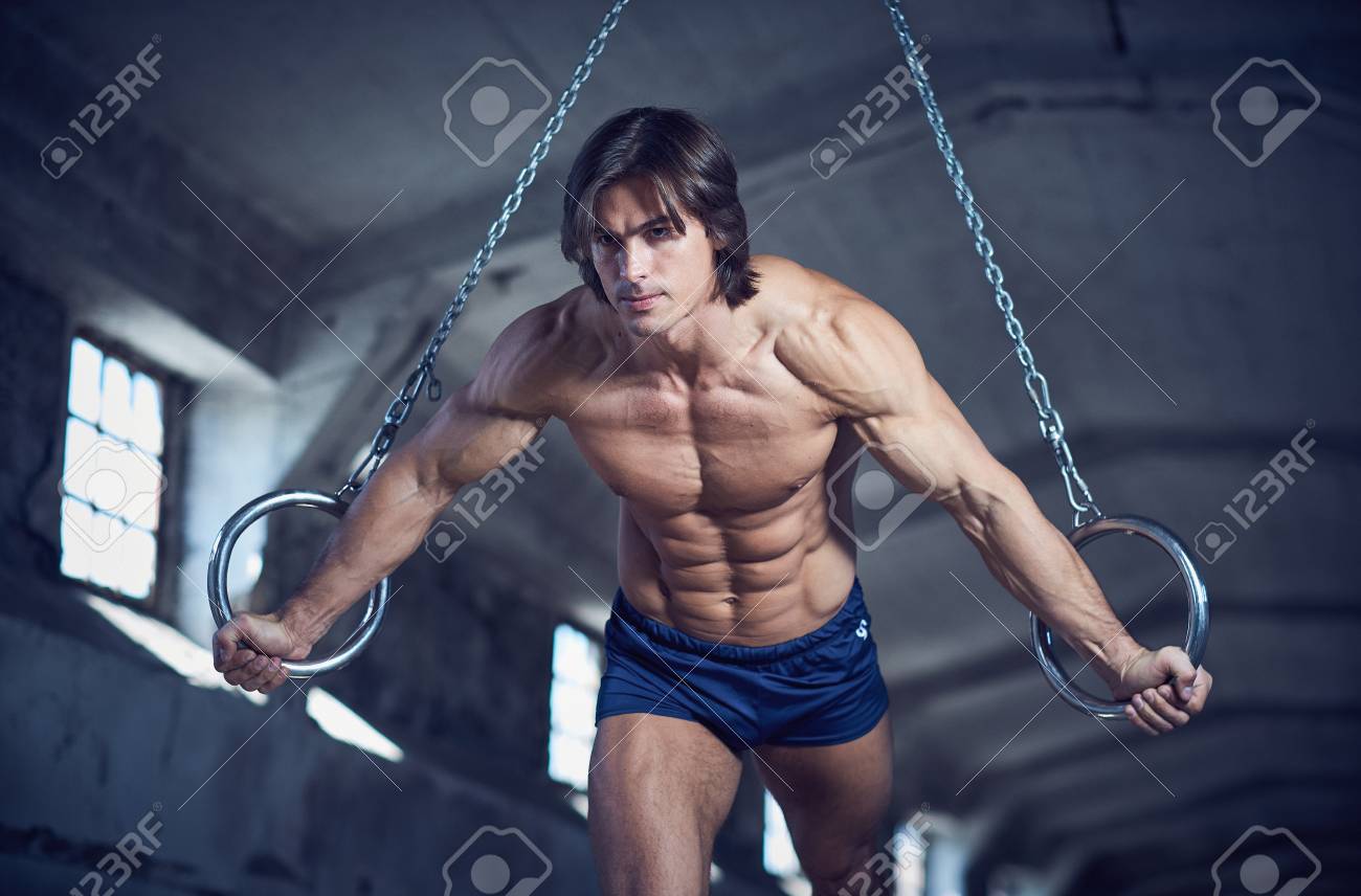 Athletic muscular male posing with gymnastic rings in a dark