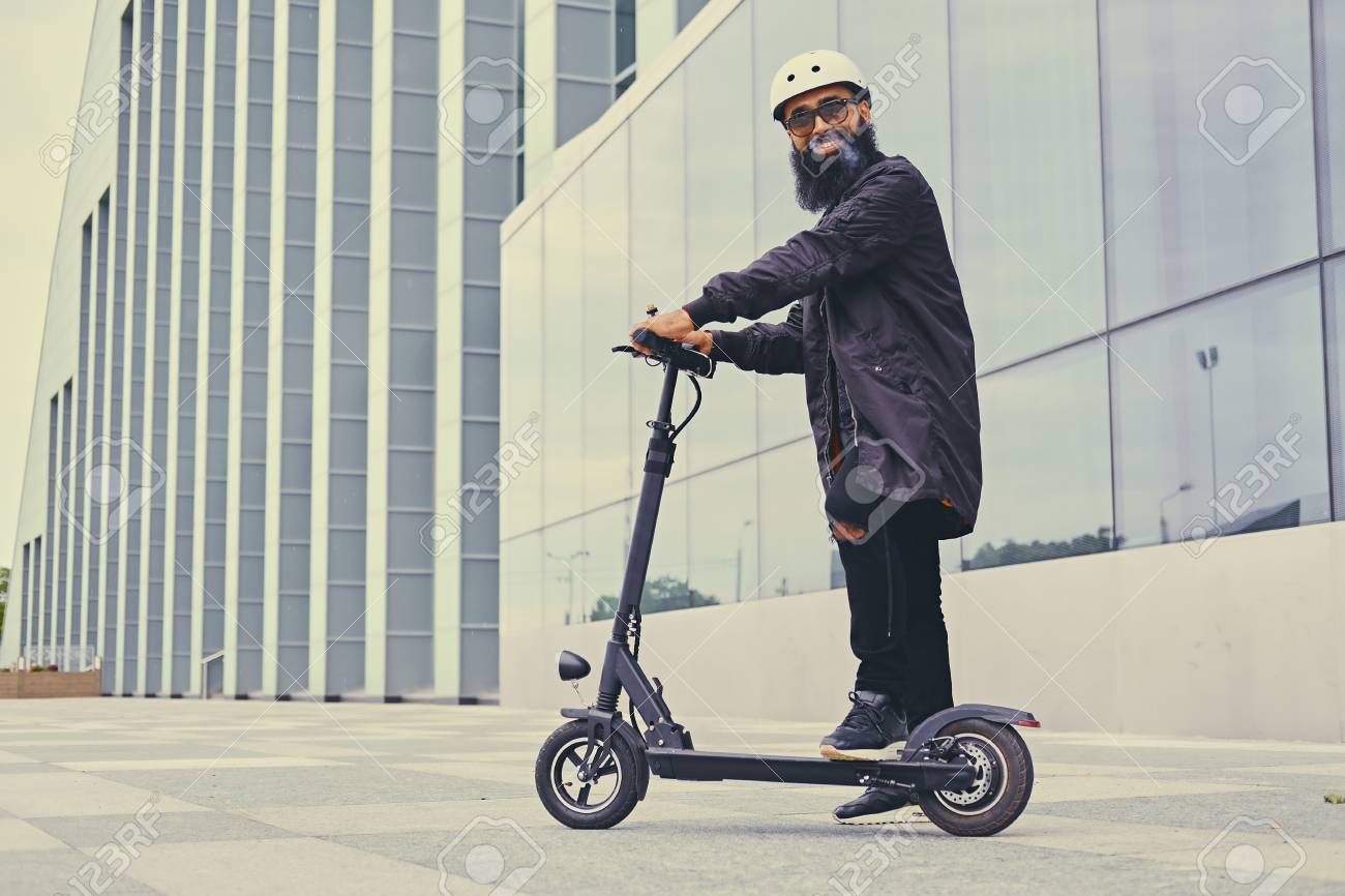 Bearded hipster male vaping and riding by electric scooter over modern building. - 86784954 Bearded hipster male vaping and riding by electric scooter over modern building. - 86784954