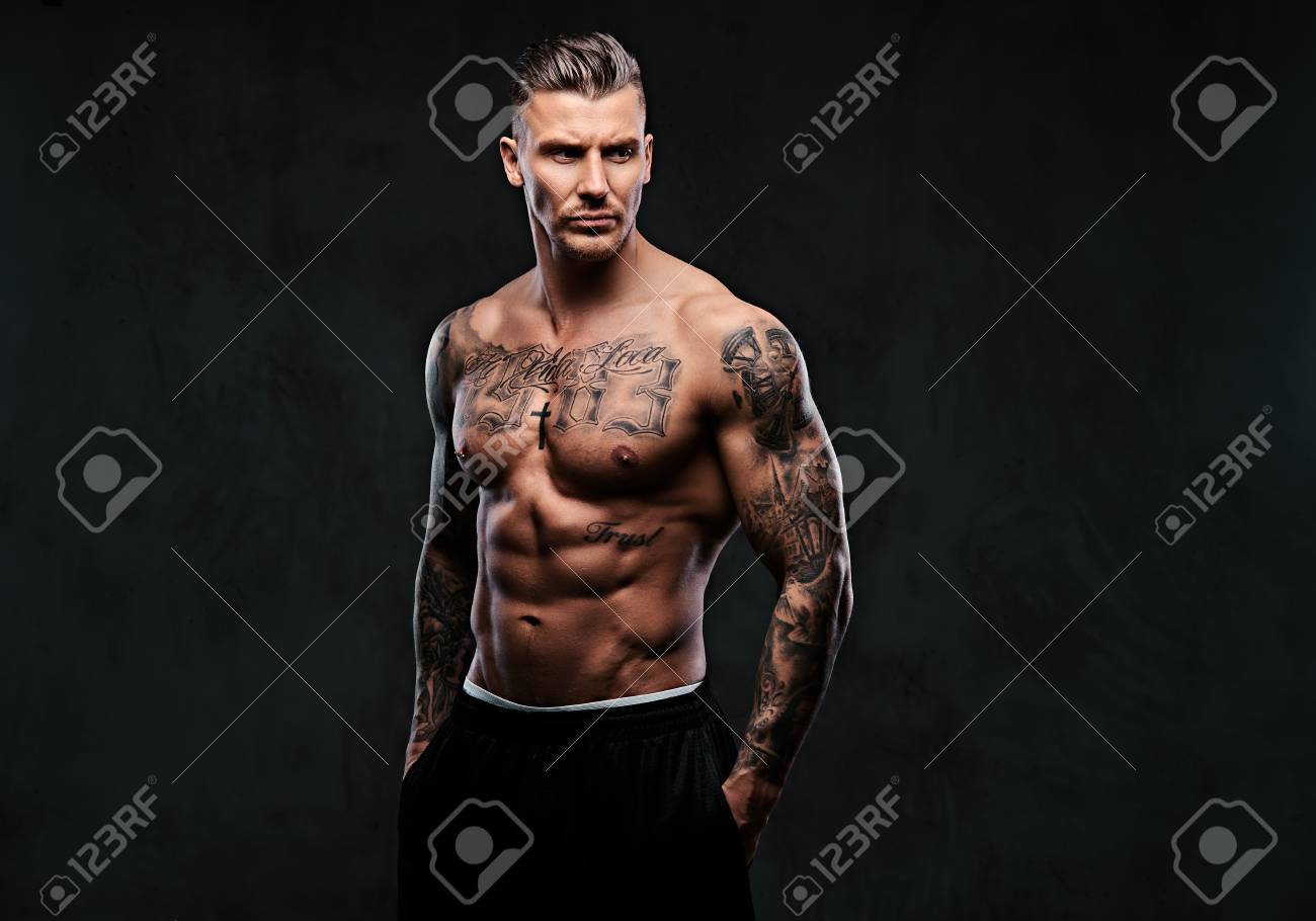 A muscular tattooed man on a dark background. - 93559352 A muscular tattooed man on a dark background. - 93559352