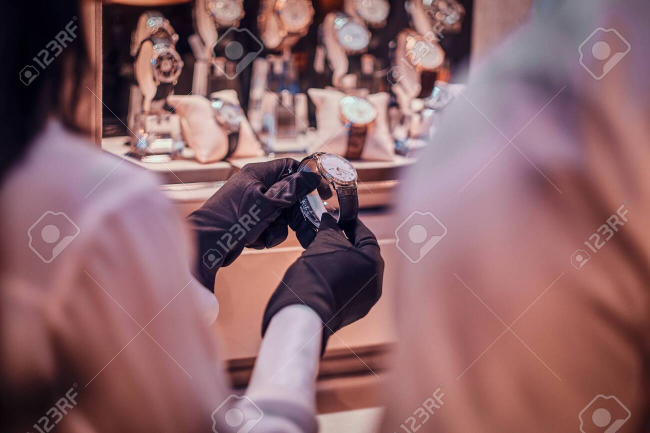 Shop assistant in black gloves is showing expensive watch for a customer. - 122080422 Shop assistant in black gloves is showing expensive watch for a customer. - 122080422