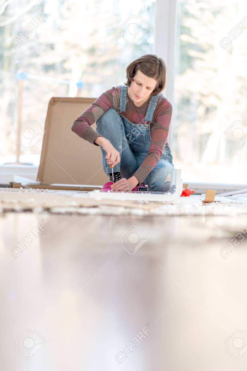 自宅の Diy 修理を行う女性は 材料や道具 ドライバーの操作に囲まれた明るいガラス窓の前の床にひざまずいてください ドライバーに焦点を当てます の写真素材 画像素材 Image