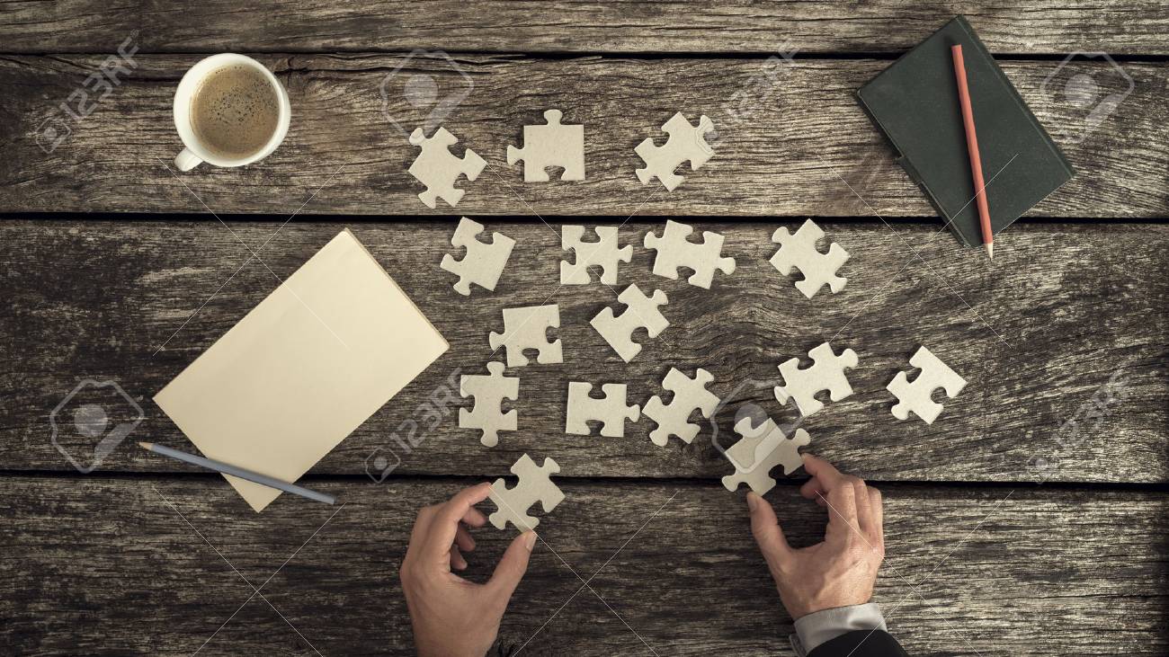 Retro style image of male hands in business suit trying to find a solution to a problem by arranging and matching puzzle pieces on a textured rustic wooden desk, top view. - 81808906 Retro style image of male hands in business suit trying to find a solution to a problem by arranging and matching puzzle pieces on a textured rustic wooden desk, top view. - 81808906