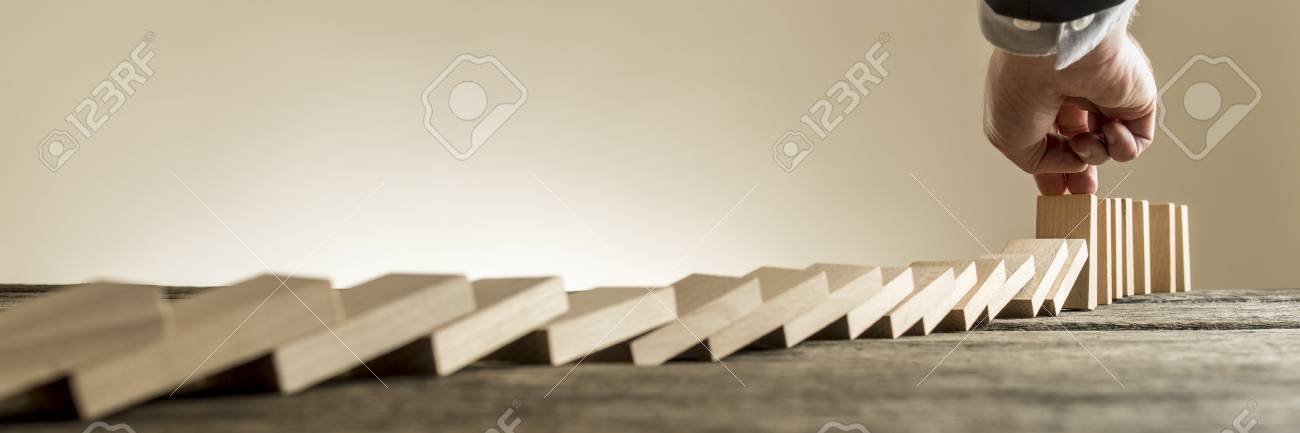 Male hand in business suit stopping domino effect of wooden blocks for concept about strategy and assistance, wide low angle view. - 82248507 Male hand in business suit stopping domino effect of wooden blocks for concept about strategy and assistance, wide low angle view. - 82248507
