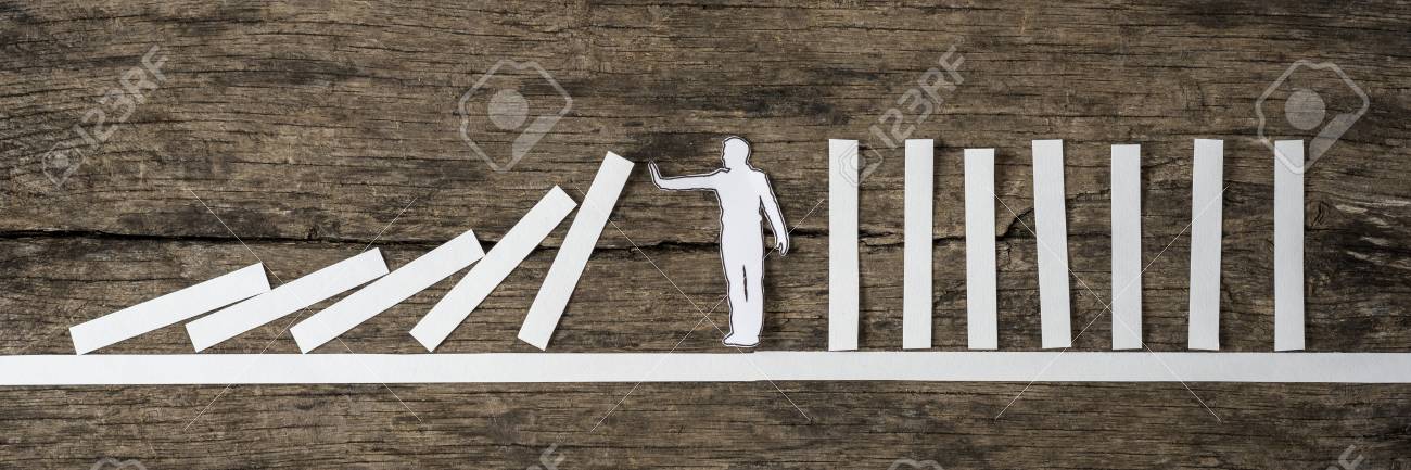 Man stopping the domino effect in a conceptual image of a white paper cutout silhouette on a rustic wood background. - 86028321 Man stopping the domino effect in a conceptual image of a white paper cutout silhouette on a rustic wood background. - 86028321