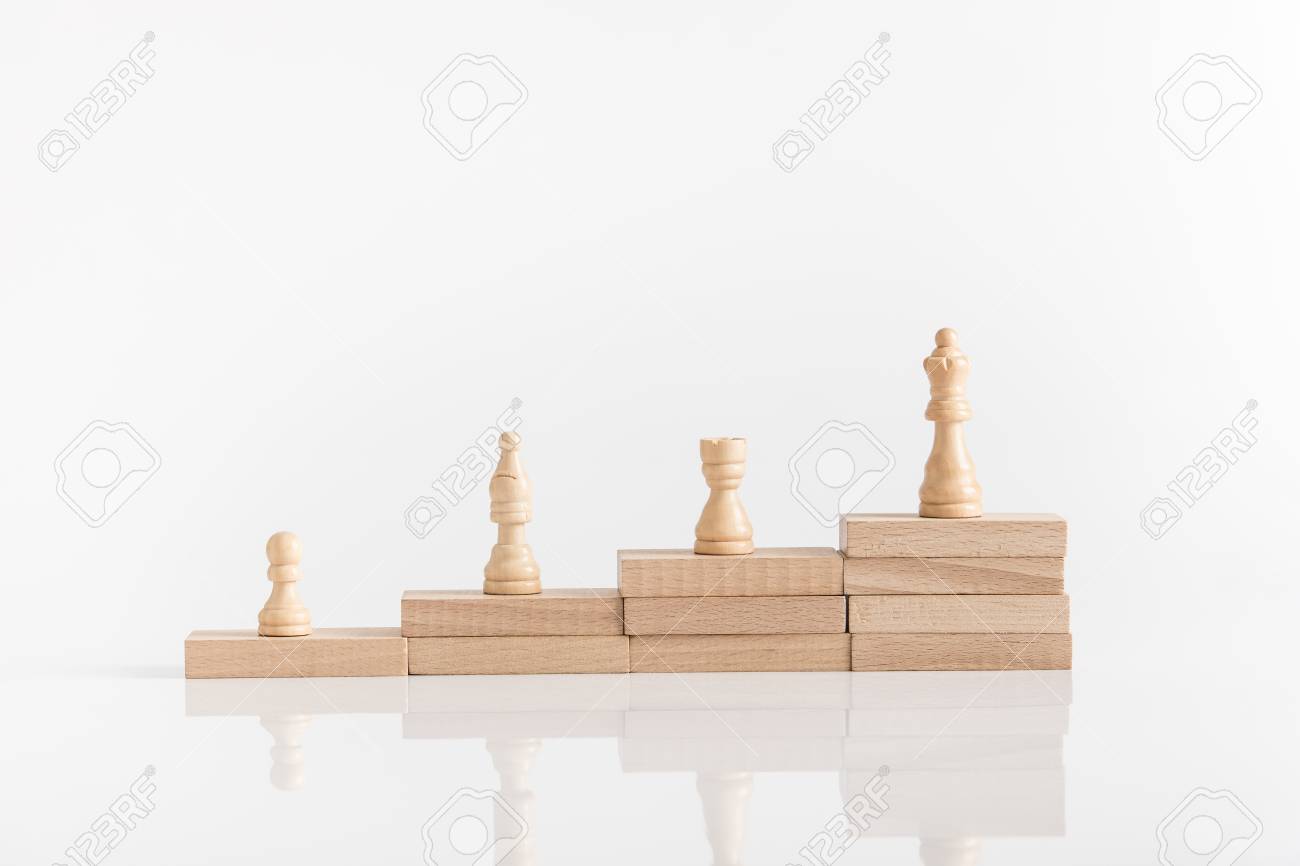 White chess pieces on a stepped stack of wooden blocks with queen piece on the highest level in conceptual image. - 106394688 White chess pieces on a stepped stack of wooden blocks with queen piece on the highest level in conceptual image. - 106394688