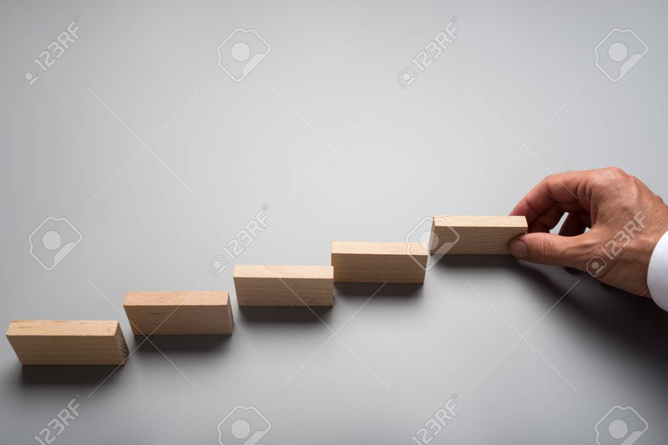 Businessman placing wooden pegs or dominos on grey surface. Conceptual of business vision and start up. - 109027078 Businessman placing wooden pegs or dominos on grey surface. Conceptual of business vision and start up. - 109027078