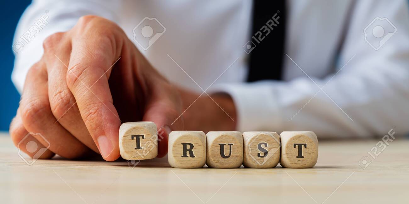 Hand of a businessman assembling the word Trust spelled on wooden dices. - 131447017 Hand of a businessman assembling the word Trust spelled on wooden dices. - 131447017