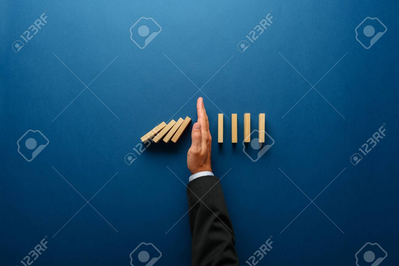 Top view of businessman hand stopping falling dominos in a business crisis management conceptual image. - 131447076 Top view of businessman hand stopping falling dominos in a business crisis management conceptual image. - 131447076