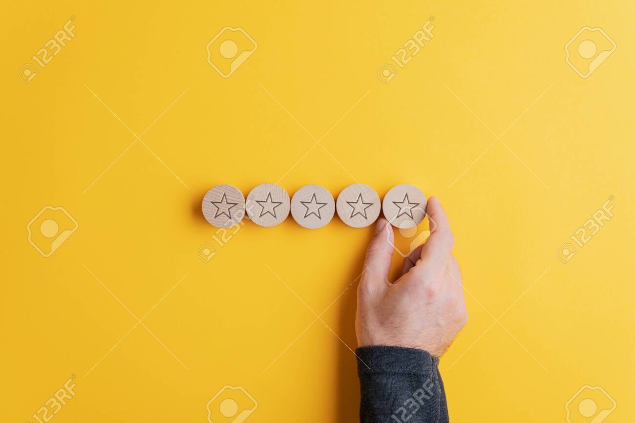 Male hand placing five wooden cut circles with stars on them in a row over bright yellow background. Conceptual image of quality and service. - 134018182 Male hand placing five wooden cut circles with stars on them in a row over bright yellow background. Conceptual image of quality and service. - 134018182