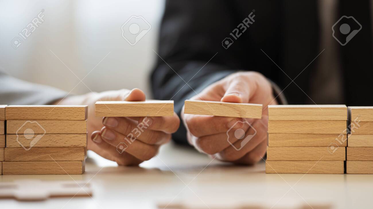 Closeup view of businessman and businesswoman making a bridge of wooden blocks between two stacks of them in a conceptual image of merger and cooperation. - 150068923 Closeup view of businessman and businesswoman making a bridge of wooden blocks between two stacks of them in a conceptual image of merger and cooperation. - 150068923