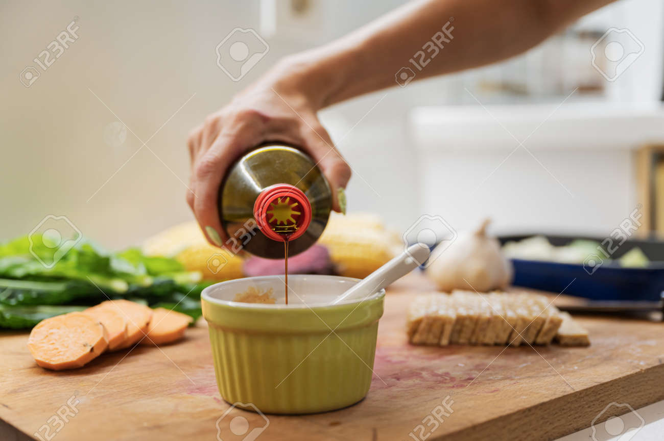 Closeup view of a woman pouring soya sauce into a cup to prepare a dip on wooden cutting board full of vegetables and vegan protein. - 169239394 Closeup view of a woman pouring soya sauce into a cup to prepare a dip on wooden cutting board full of vegetables and vegan protein. - 169239394