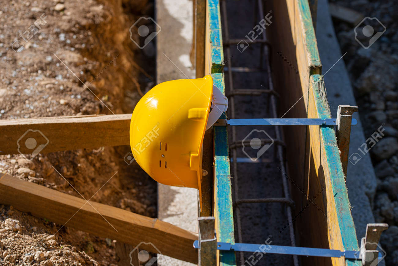 Yellow protective hardhat resting on a framework of wooden panels in a construction site. - 169239400 Yellow protective hardhat resting on a framework of wooden panels in a construction site. - 169239400