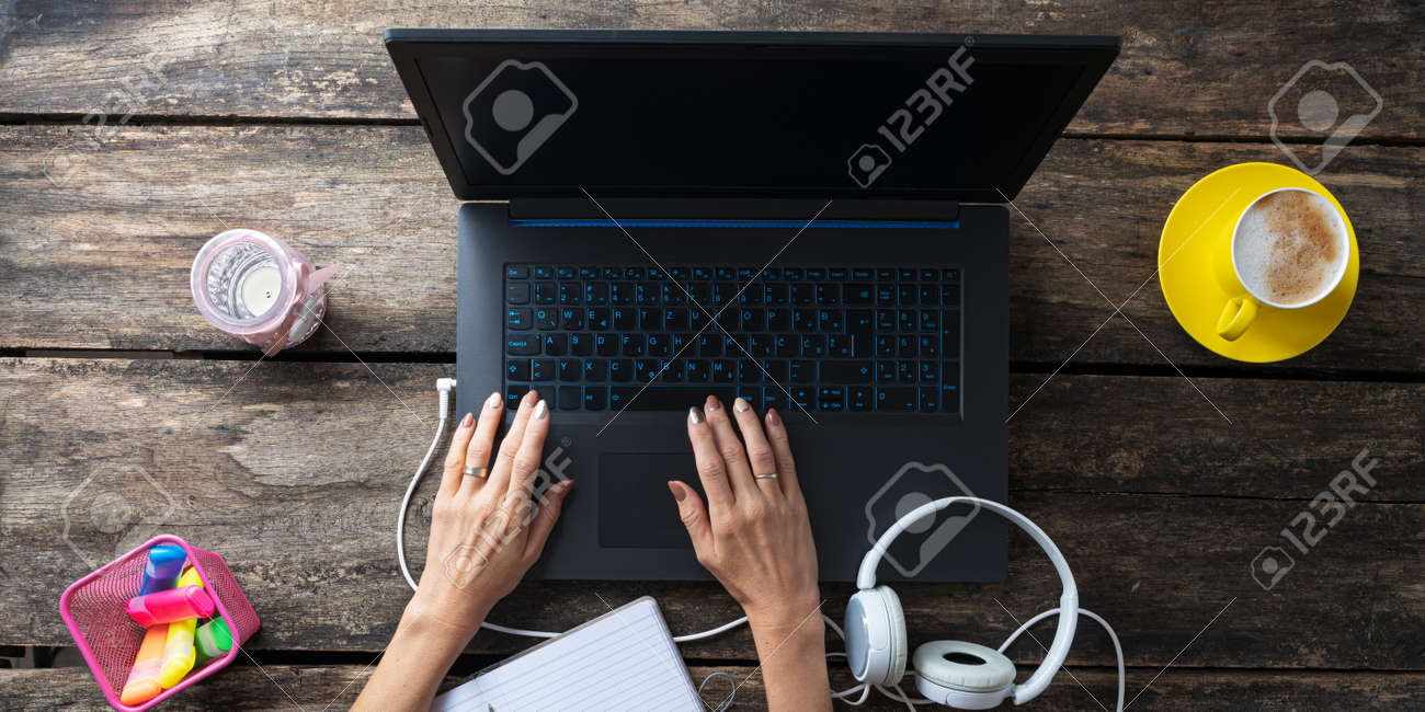 Top view of female student working on laptop computer with headphones, colorful markers and cup of coffee beside it on the table. - 169239401 Top view of female student working on laptop computer with headphones, colorful markers and cup of coffee beside it on the table. - 169239401