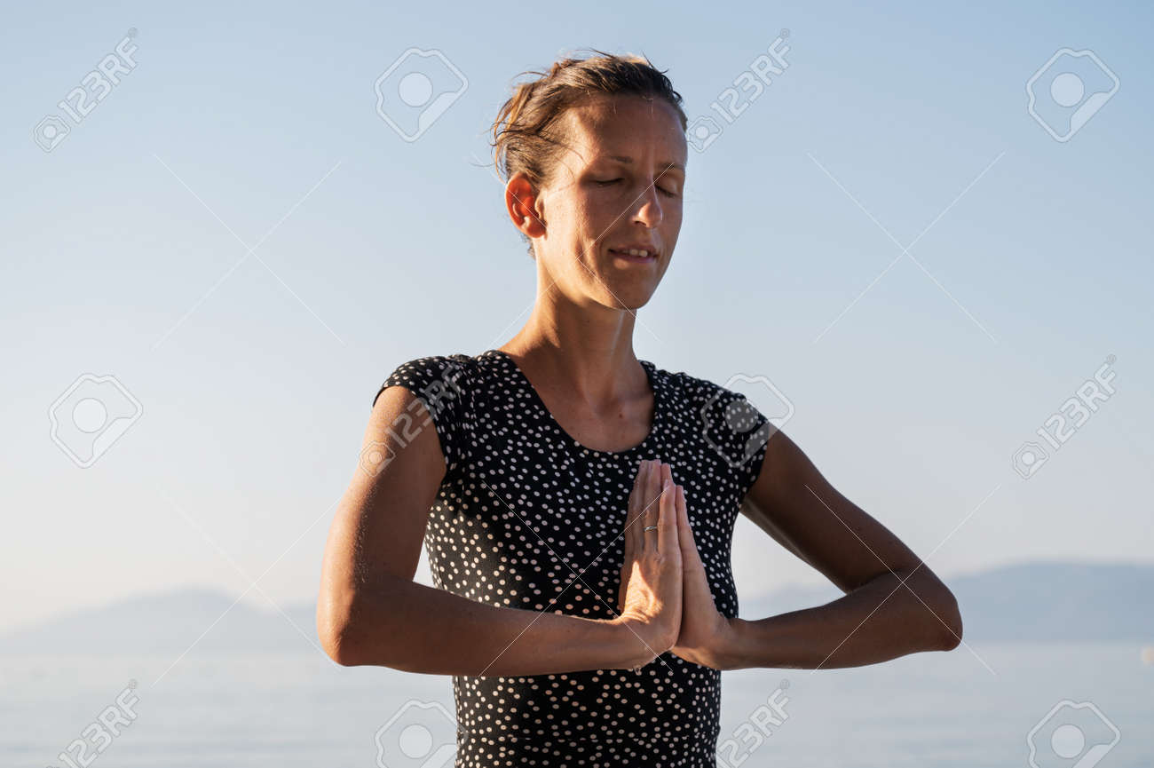 Young woman with the palms of her hands joined in front of her chest meditating by the sea. - 169239404 Young woman with the palms of her hands joined in front of her chest meditating by the sea. - 169239404