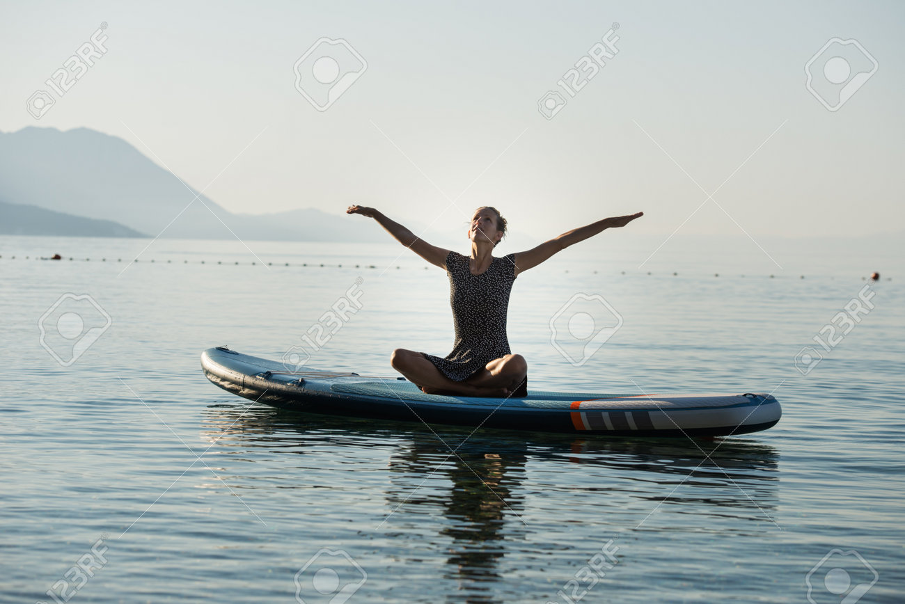 Young woman celebrating life practicing yoga on sup board floating on calm morning sea water. - 170456455 Young woman celebrating life practicing yoga on sup board floating on calm morning sea water. - 170456455